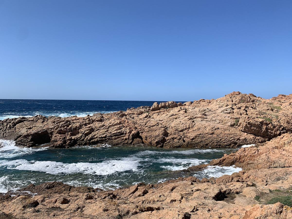 Spiaggia di Isola Rossa con acque blu e costa rocciosa della Sardegna